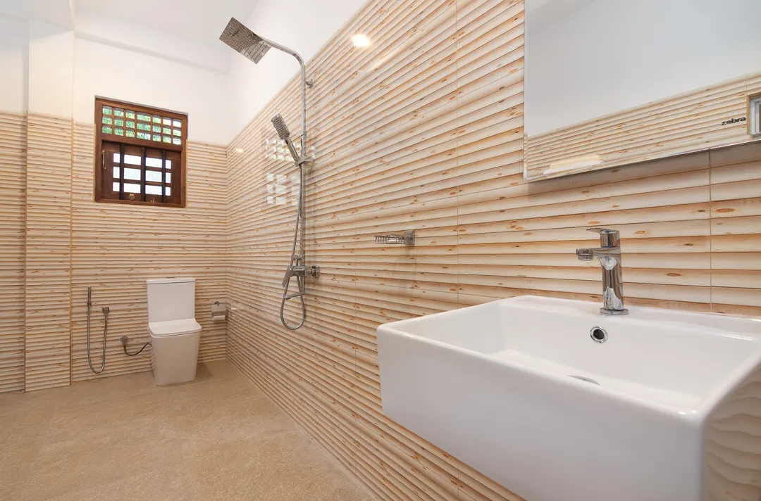 A bathroom with striped wall tiles, a rain shower and a wide basin