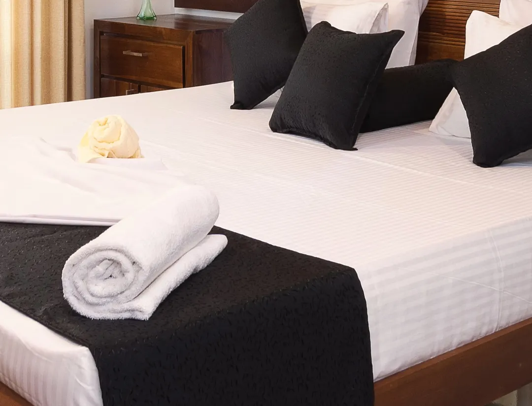 Rolled towels on white linen at the foot of a king bed