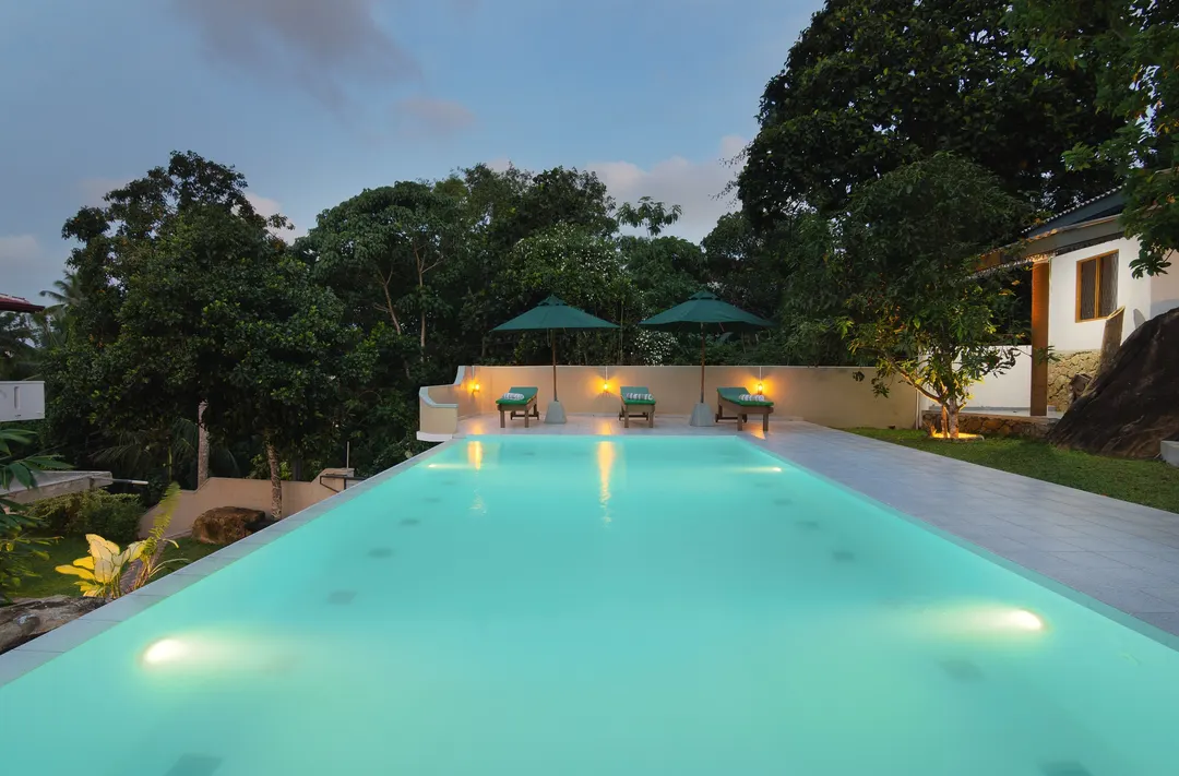 The pool lit at dusk, the length of the garden, with lamps on the far wall