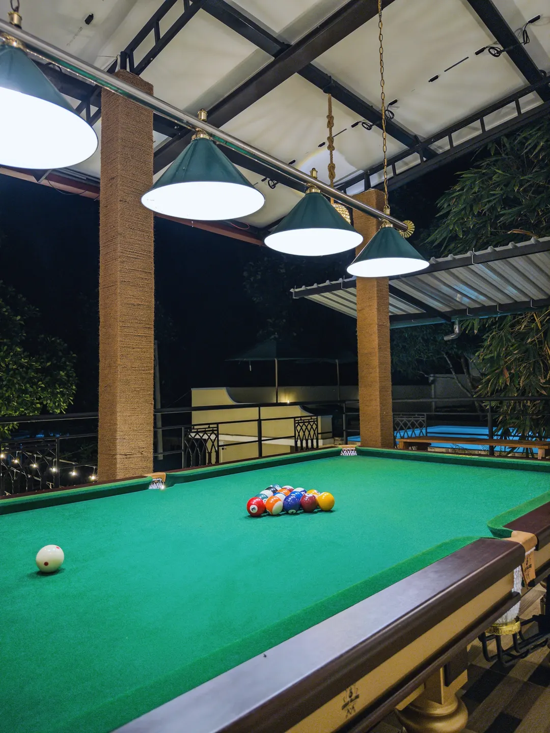 The pool table on the covered terrace at night, string lights along the rail