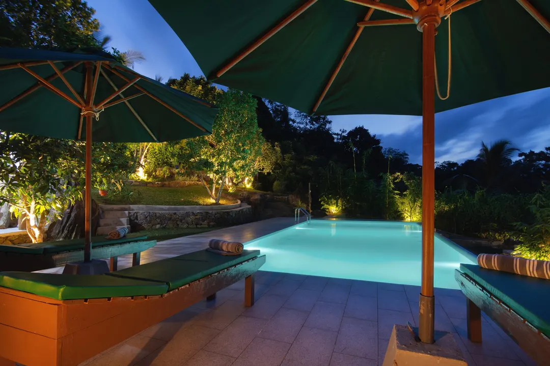 Green umbrellas and loungers beside the lit pool at blue hour
