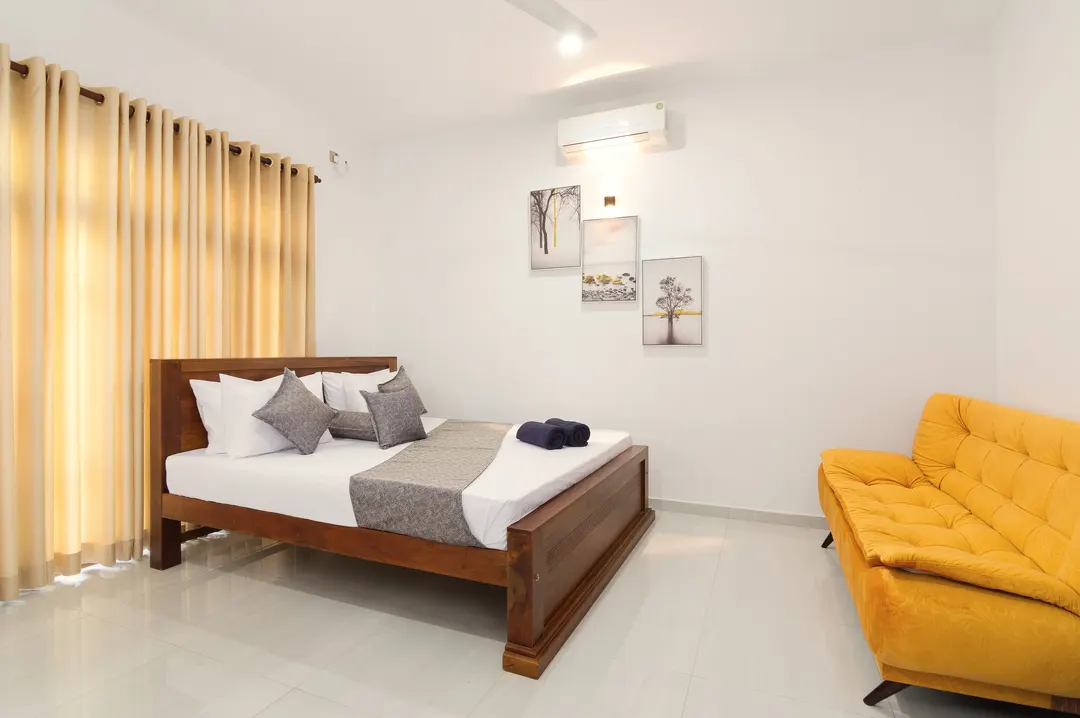 A Deluxe Triple with a king bed and a yellow sofa bed, framed prints on the wall