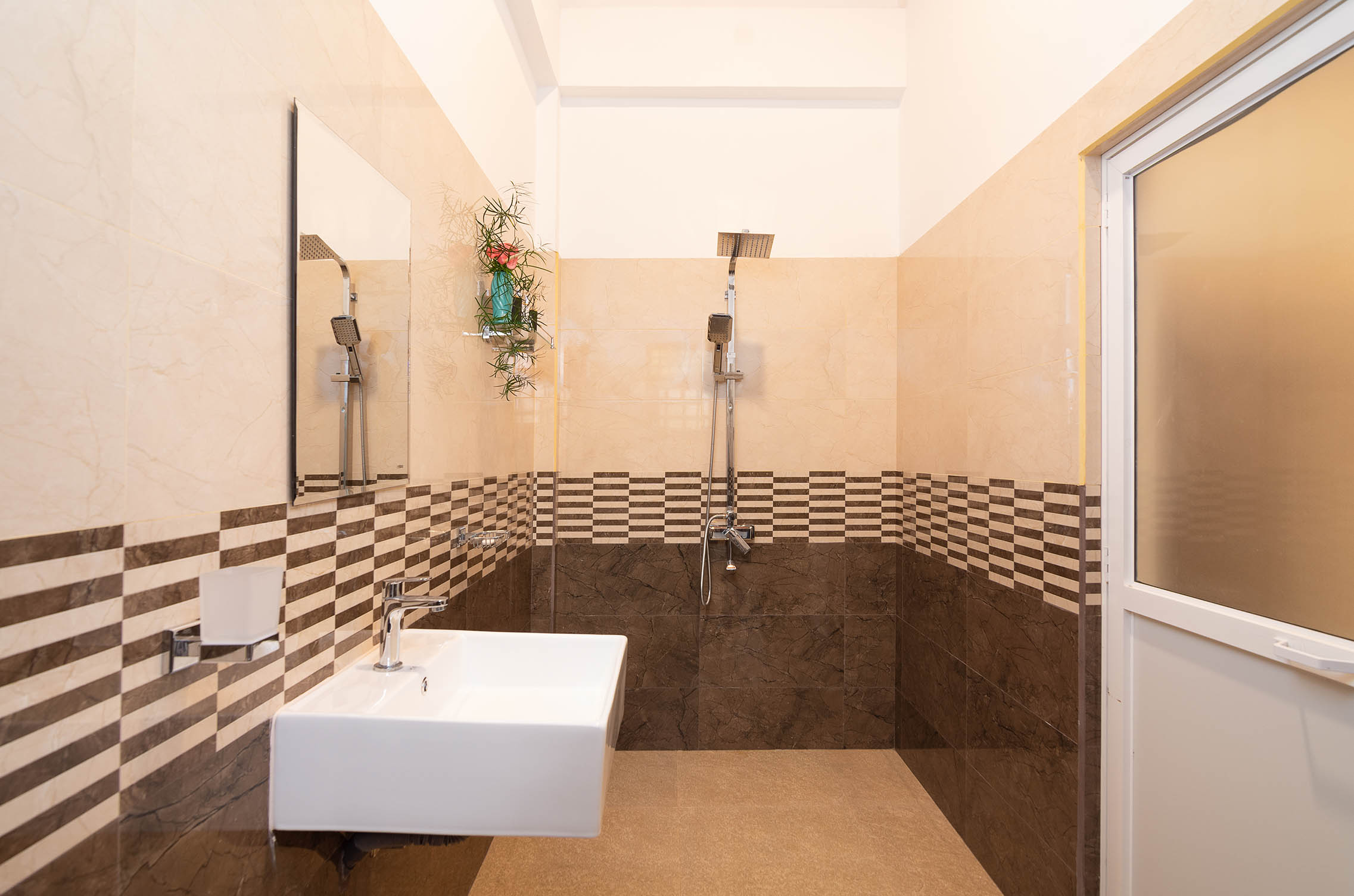 Modern villa bathroom with stylish tiling, rainfall shower, and sleek white sink for a luxurious and refreshing experience."