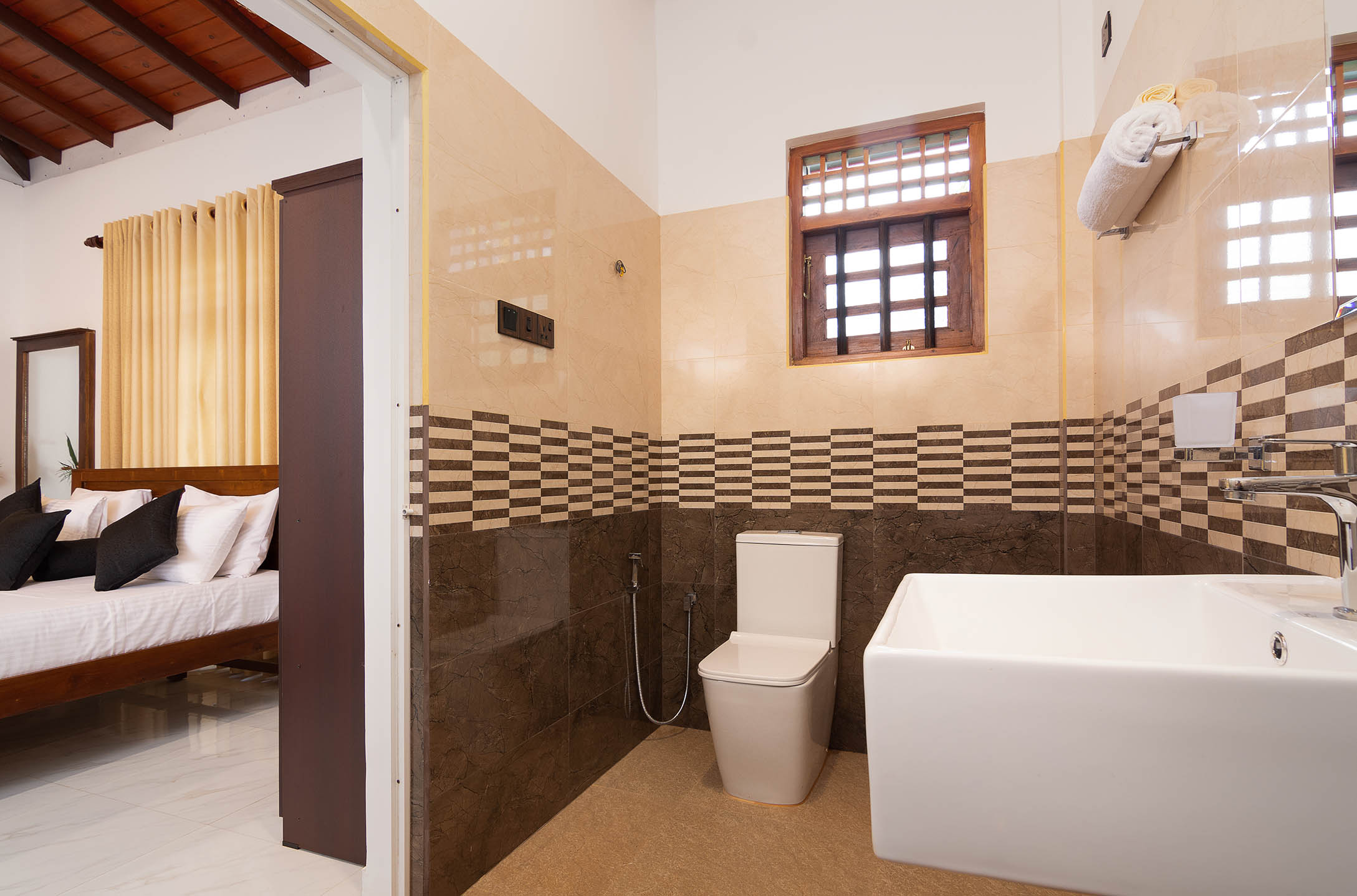 Luxurious villa room with a king-sized bed and an adjacent modern bathroom featuring elegant tiling, located in a serene setting.