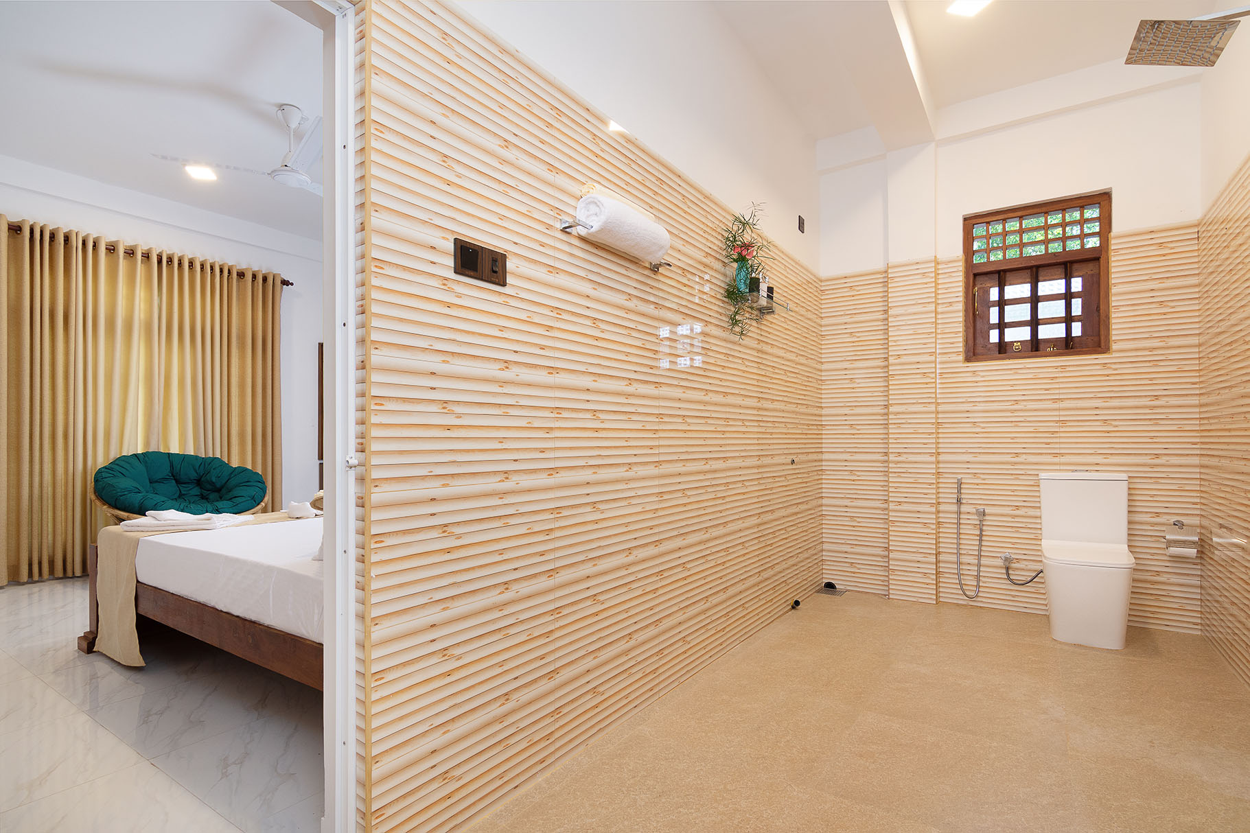 Modern bedroom interior at Tranquil Escape Villa in Hikkaduwa, featuring a wooden slatted wall divider, a single bed with white bedding and a green cushion, and an open bathroom area with light-colored tile flooring