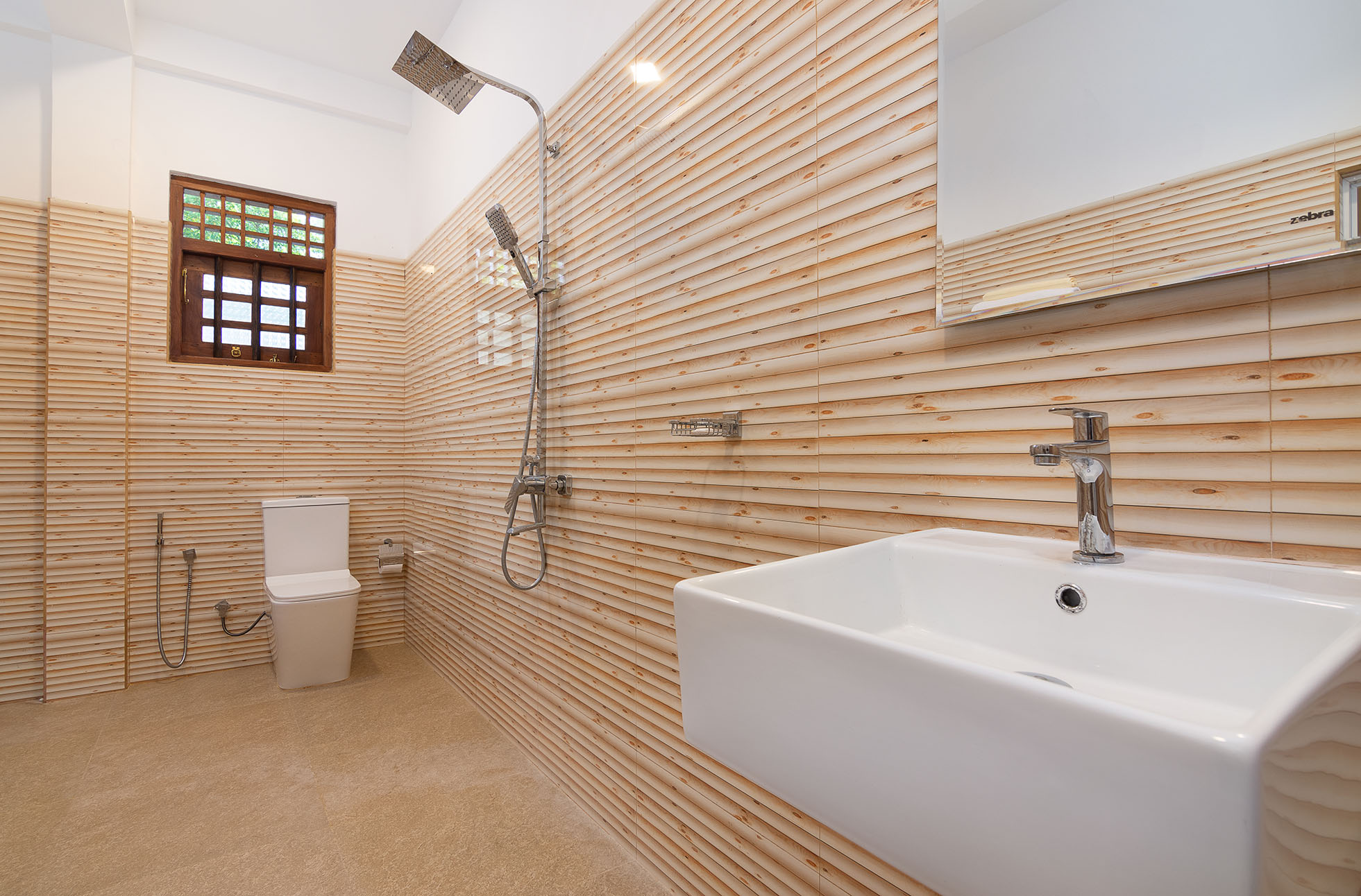 Modern bathroom at Tranquil Escape Villa in Hikkaduwa, featuring light wooden panel walls, a white ceramic sink with a silver faucet, a toilet, and a walk-in shower with both rainfall and handheld showerheads.