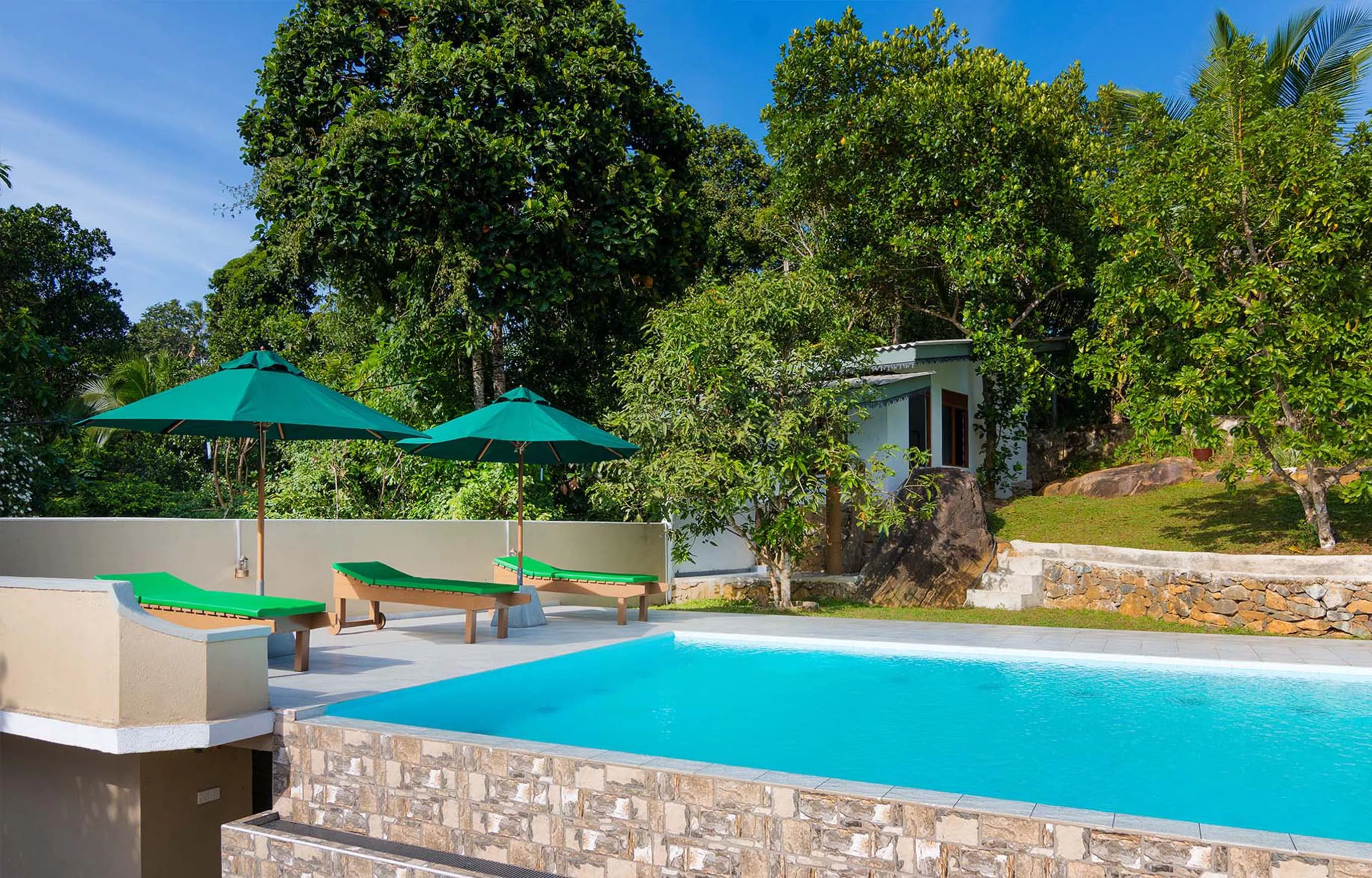 Tranquil pool area at a luxury villa in Hikkaduwa, Sri Lanka. Relax on sun loungers under shaded umbrellas and enjoy the stunning views of the surrounding tropical landscape.