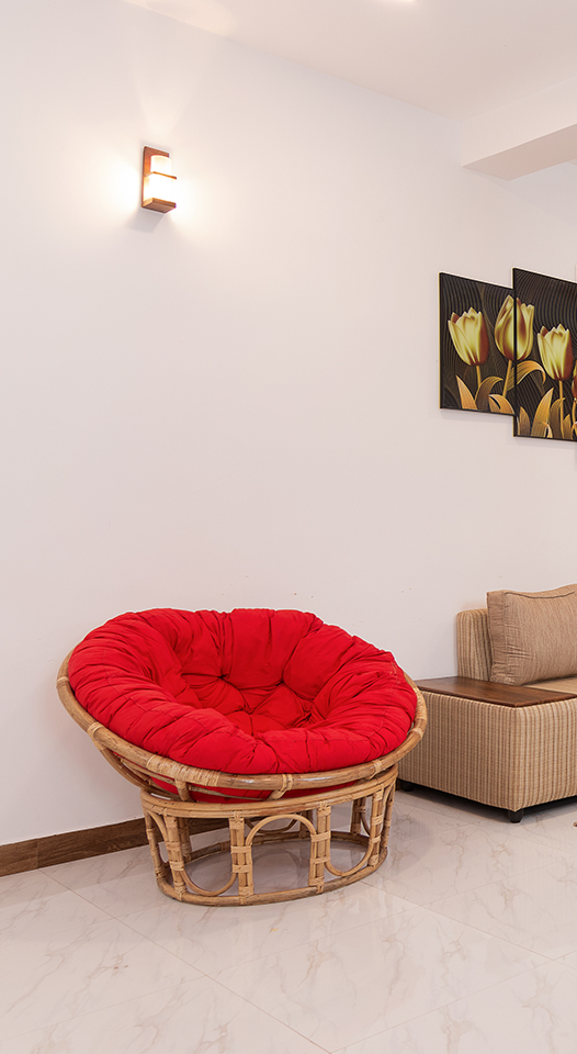 Spacious and well-lit living room featuring a modern beige sectional sofa, vibrant red cushioned round chair, and artistic three-panel golden flower artwork on the wall. Ideal for home decor inspiration and real estate listings.