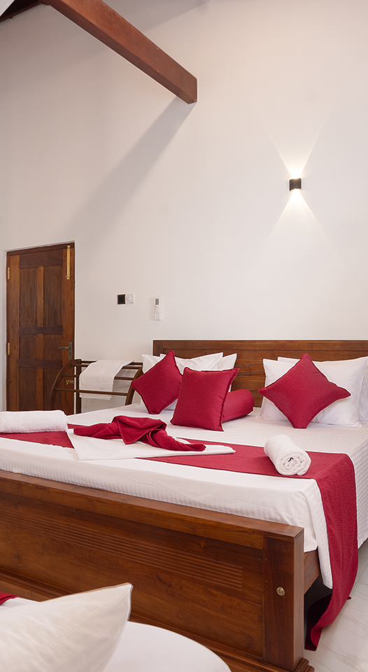 A beautifully designed bedroom with a wooden king-size bed, adorned with white and red bedding, complemented by a matching single bed. The room has high ceilings with exposed wooden beams and contemporary wall décor, creating a warm, inviting atmosphere.