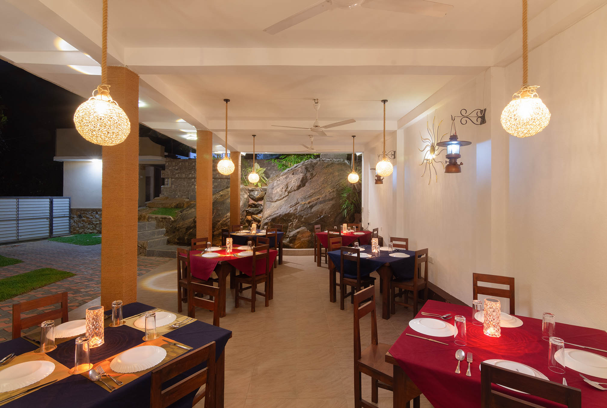 Tranquil Escape Hikkaduwa: Elegant outdoor dining area with ambient lighting, featuring colorful table settings, wooden furniture, and a dramatic boulder backdrop, perfect for intimate dinners