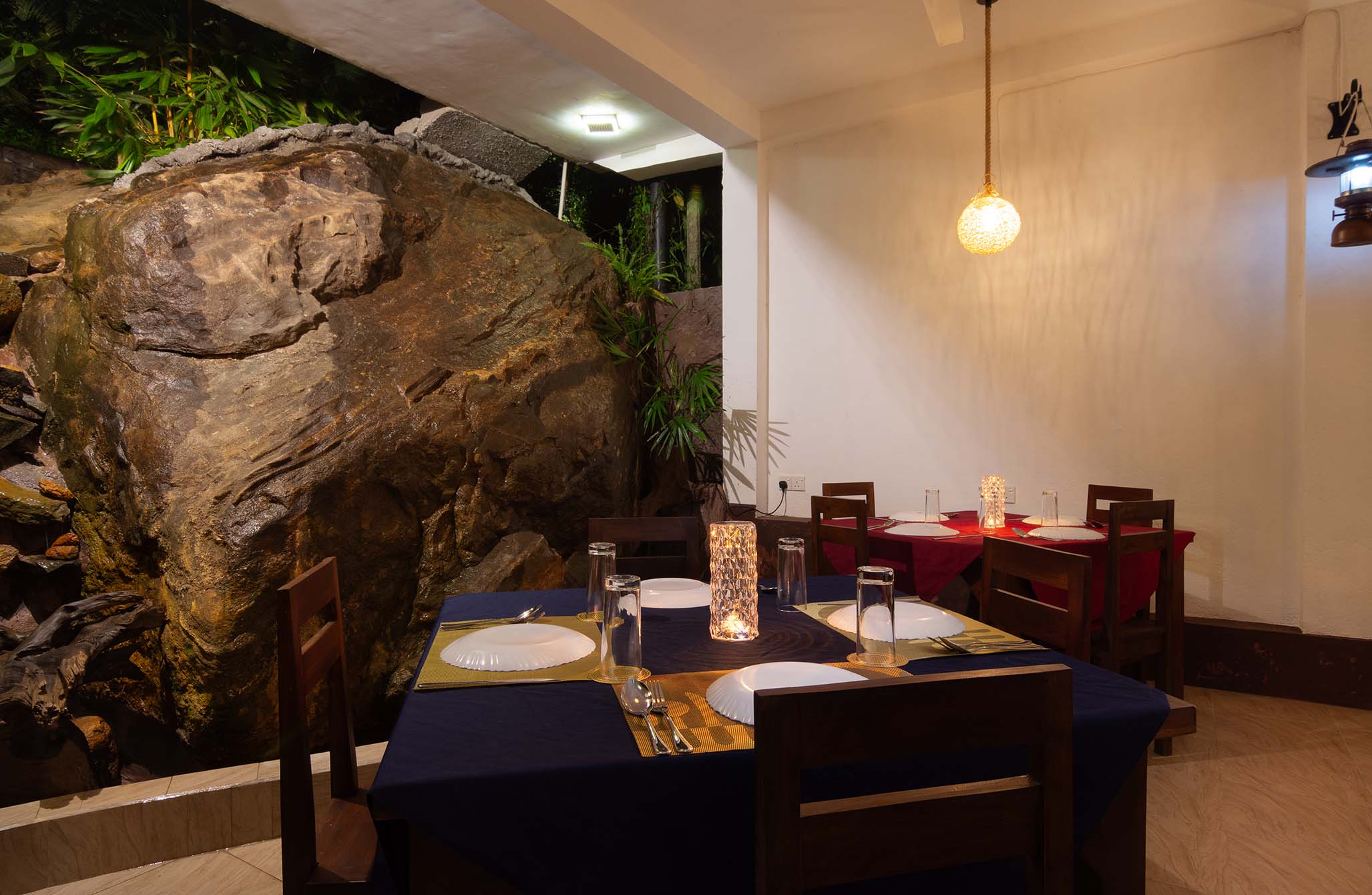 Tranquil Escape Hikkaduwa: Unique dining experience with tables set against a natural rock formation, complemented by warm lighting and tropical plants, offering an immersive fusion of nature and luxury